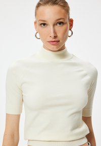 Crème-kleurige aansluitende top met korte mouwen, een hoge hals, ribbelstructuur en raglanmouwen, ontworpen voor een strakke pasvorm.