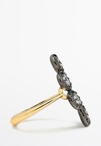 Bague en or et noir avec un design en T-barre ornée de cristaux clairs facettés et des détails complexes le long des bords. Finition métallique lisse.