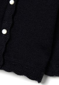 Cardigan blu scuro con una morbida texture a maglia, orlo ondulato e bottoni bianchi che si allineano sul davanti per la chiusura.