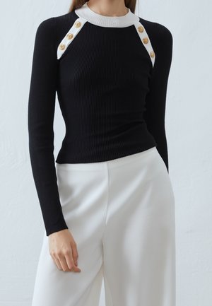 Top nero a maniche lunghe a coste con colletto bianco e bottoni dorati abbinato a pantaloni bianchi a vita alta e gamba larga.