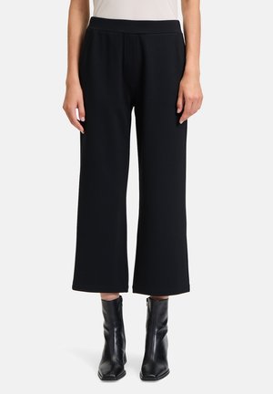 Pantaloni neri a gamba larga realizzati in un tessuto morbido e testurizzato con vita alta. Indossati con stivaletti neri alla caviglia, che mettono in risalto una silhouette pulita e moderna.