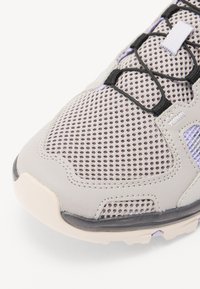 Hellgrauer Sportschuh mit Mesh-Obermaterial, schwarzen Schnürsenkeln, lila Akzenten und Gummisohle. Gepolsterter Schuhkragen für zusätzlichen Komfort. Strukturiert Oberfläche.