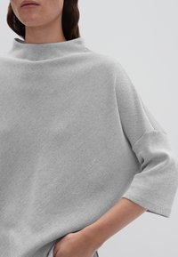 Grauer gerippter Stricktop mit hohem Kragen und Dreiviertelärmeln; zeichnet sich durch einen lockeren Schnitt und eine weiche Textur aus, die für Komfort sorgt.