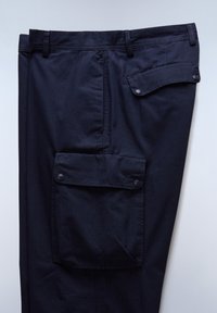 Marineblauwe broek met een gladde textuur, voorzien van een voorzak met een flap en drukknoopsluiting, en een zijpatchzak met knopen.