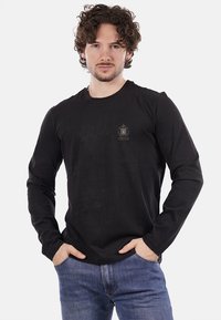 Maglietta nera a maniche lunghe realizzata in tessuto liscio, con un piccolo logo sul petto. Abbinata a jeans di denim azzurro chiaro.