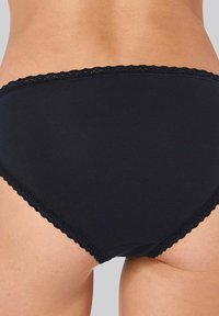 Schwarze Baumwollunterhose mit gewelltem Spitzebesatz am Bund und den Beingrößen. Glatte Textur und hohe Taillenschnitt für vollständige Abdeckung.