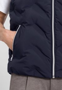 Marinefarbener Steppweste mit einem Reißverschluss vorne, Seitentaschen und einer glatten, isolierten Textur. Mit silbernen Reißverschlüssen und einer taillierten Passform.