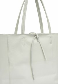 Borsa tote in pelle bianca con superficie testurizzata, dotata di due manici lunghi e dettaglio annodato nella parte superiore. Design minimalista, senza ulteriori accenti.