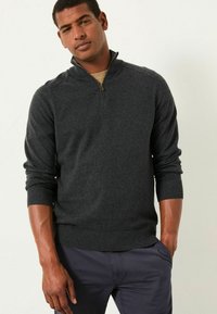 Dunkelgrauer Quarter-Zip-Pullover aus Strickstoff mit gerippten Bündchen und Saum. Verfügt über einen Reißverschluss mit goldfarbener Hardware. Getragen über einem hellen Hemd.