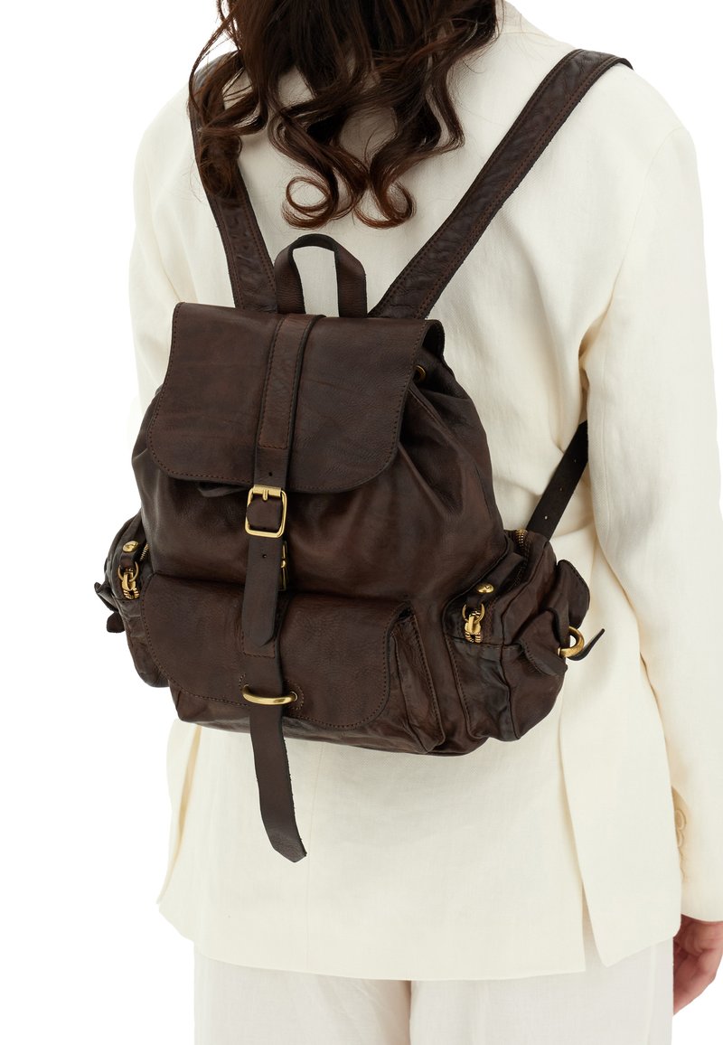 Zaino in pelle marrone con pattina, spallacci regolabili, finiture in oro, tasche con zip e una finitura testurizzata. Design compatto e pratico.
