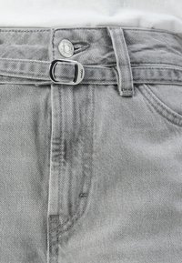 Grå denimbukser med metallknapp og løftedetaljer, med en linning med beltehemper og subtil stikning langs sømmene.