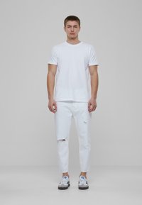 Valge puuvillane T-särk, lühikeste varrukatega; kulunud valged teksad, millel on rebenemised; mustad ja valged tennisetossud siniste aktsentidega. Lihtne, igapäevane disain.