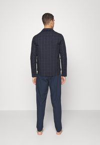 Camisa de patrón marino con diseño de cuadrícula, mangas largas y cuello liso, combinada con pantalones navy a juego. Textura minimalista y suave.