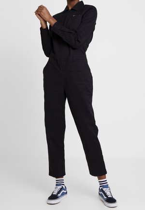 Sort jumpsuit med lange ærmer og krave, med lynlås og sidelommer. Pyntet med en lille broderet logo.