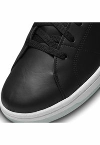 Sneaker in pelle nera con una texture liscia, punta tonda, chiusura con lacci e suola in gomma bianca con un delicato accento verde menta.