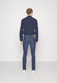 Camisa de manga larga navy combinada con jeans ajustados de color azul oscuro. Los jeans tienen bolsillos traseros y un parche de cuero marrón en la cinturilla.