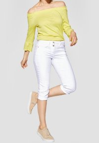 Geel off-shoulder top met gerimpelde mouwen, gecombineerd met witte capri-pantalons en beige geknoopte schoenen. Eenvoudig ontwerp, lichte stof.
