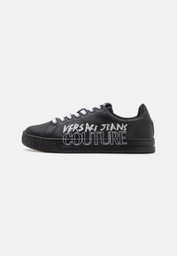 Czarny sneaker z gładką skórzaną fakturą, białymi sznurówkami i dużym napisem "Versace Jeans Couture" wydrukowanym na boku. Gruba podeszwa.