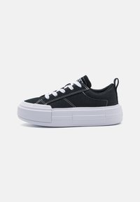 Sorte kanvas-sneakers med hvite lisser, en kraftig hvit såle og kontraststing. Har en drahank på hælen for enkel påkledning.