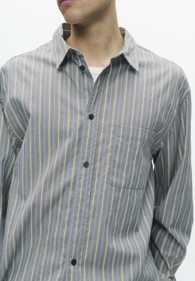 Srajca s potiski z gumbi, iz mehkega bombažnega blaga; ima modre, sive in rumene črte, prsni žep in črne gumbe.