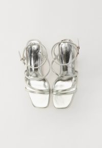 Sølvhelte sandaler med en skinnende metallisk finish. Har flere tynne stropper med spenneinnfell og et firkantet tådesign.