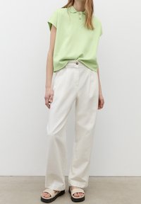 Jasnozielona koszulka polo z krótkimi rękawami i kołnierzykiem, w zestawie z szerokimi białymi spodniami i neutralnymi sandałami z grubą podeszwą.