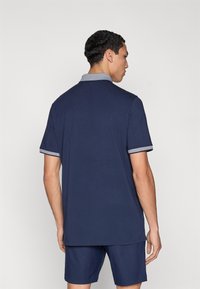 Μπλε ναυτικό πόλο μπλουζάκι με κοντά μανίκια και γιακά με αντίθετο μοτίβο. Ομαλή υφή, κλασικός σχεδιασμός και ίσια γραμμή. Φοριέται με ταιριαστά σορτς.