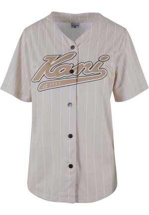 Beige kortærmet jersey med hvide lodrette striber, der har en knaplukning foran og ordet "Kani" fremtrædende vist i brune bogstaver.