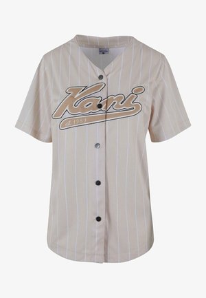 Bežinė trumpomis rankovėmis džersio medžiagos maikutė su baltomis vertikaliomis juostelėmis, su užsegimu priekyje ir žodžiu "Kani", ryškiai išspausdintu ruda spalva.