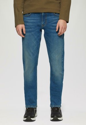 Jeans de mezclilla azul con un corte slim, efecto desgastado, diseño de cinco bolsillos y corte recto, llevados con zapatos deportivos negros.