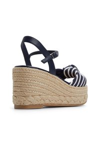 Sandale compensée avec une plateforme en jute tressé, une bride de cheville en cuir bleu marine et un dessus en textile à rayures bleu marine et blanc.