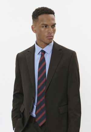 Veste de costume marron sur une chemise bleu clair, associée à une cravate à rayures diagonales bleu marine, rouge et blanche. Texture lisse, coupe ajustée.