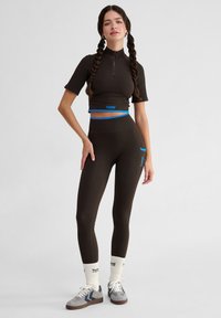 Bruine geribbelde crop top met korte mouwen en een hoge hals, gecombineerd met bijpassende high-waisted legging met blauwe accenten.