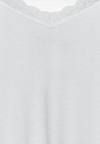Top de cuello en V en suave tela blanca, con textura acanalada y un delicado borde de encaje a lo largo del escote para un detalle adicional.
