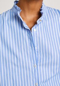 Light blue striped shirt featuring a ruffled collar, button front, and textured fabric. Stripes are alternating light and dark shades of blue.