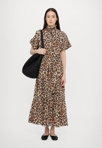 Løveprikket kjole med høy krage, korte ermer og lagdelt kant. Kombinert med en teksturert svart vevet veske og svarte flate sko.