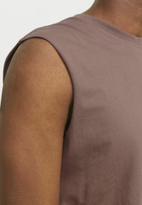 Camisa sin mangas ajustada y elegante en un suave tejido malva, que muestra una textura lisa y un escote redondo, con un sutil brillo.