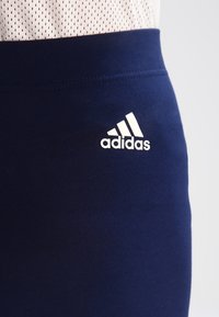 Närbild av marinblå träningstights med vitt Adidas-logotyp tryckt på övre låret, ihopparat med en vit mesh-top.