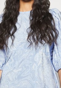 Ljusblå klänning med ett marmor mönster, puffärmar och en rynkad midja. Tillverkad av mjukt, strukturerat tyg.