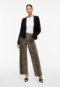 Μαύρο κασκόλ πάνω από ένα λευκό πουκάμισο, συνδυασμένο με φαρδιά leopard print παντελόνια. Το outfit έχει χαλαρό σχεδιασμό και λείο ύφασμα.