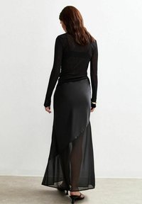 Haut à manches longues noir avec une texture transparente, associé à une jupe maxi noire asymétrique et fluide, dotée d'une finition satinée élégante.