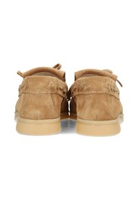 Zapatos de ante estilo mocasín en un tono marrón claro, con forma curvada, textura suave, costura decorativa en la parte trasera y suelas de goma.