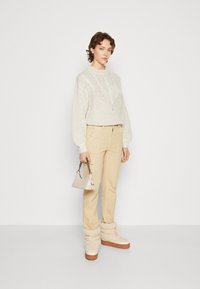 Beige strikket sweater med et struktureret mønster, lysebrune cargo-bukser, en krèmefarvet håndtaske med kædestrop, og fluffy beige platform-støvler.