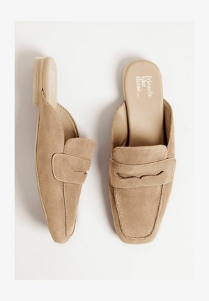 Beige ruskind mules med rund tå, lav hæl og dekorativ stropdetalje. Indersiden har teksten: "venner som disse..."