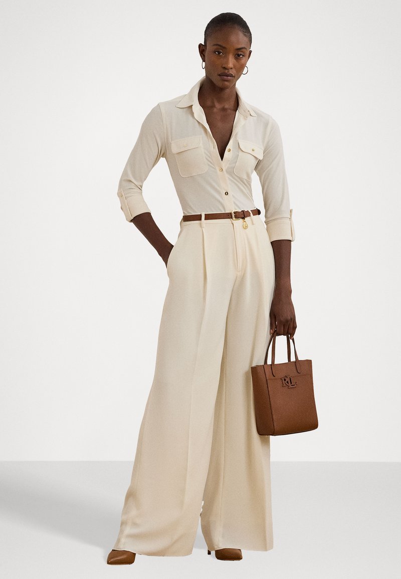 Bežinė marškinė su apykakle ir dviem krūtinės kišenėmis, derinama su grietinėlės spalvos plačiais kelnais. Rudas diržas ir rankinė, abi su tekstūrinėmis paviršiais.