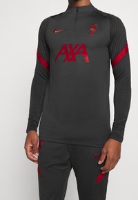 Mørkegrå træningstop med lange ærmer, med røde detaljer, en kvart lynlås og logoer for LFC og Nike. Fremstillet af struktureret stof.