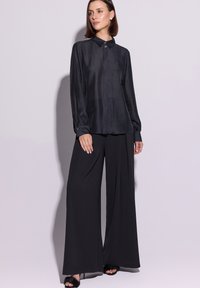 Czarna koszula z długim rękawem, kołnierzykiem i guzikami, połączona z czarnymi, szerokimi, wysokim stanem spodniami oraz czarnym obuwiem z odkrytymi palcami.