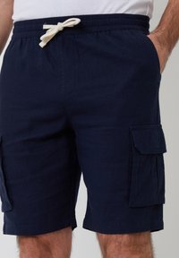 Shorts cargo navy en tissu tissé avec une taille élastique, des poches avant et des poches latérales à rabat. Dotés d'un cordon de serrage blanc.