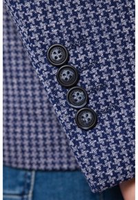 Tkanina w granatowo-błękitny wzór houndstooth zbliżenie czterech czarnych guzików na mankiecie szytej marynarki.