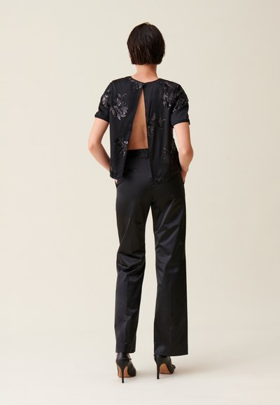 Top nero con ricami floreali e schiena scoperta, abbinato a pantaloni neri eleganti. L'insieme presenta una texture liscia e una forma aderente.